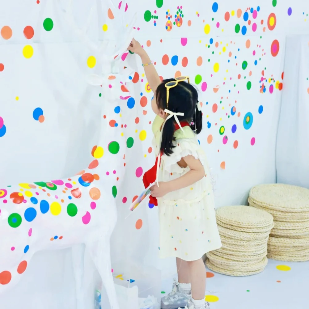 Child adding colorful dots to a white art display